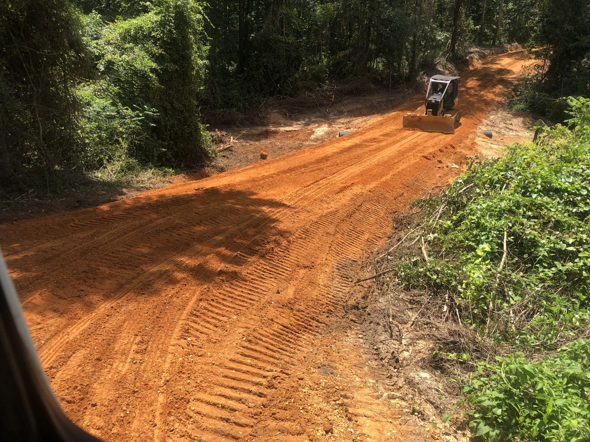 Dozer grading a new red clay road cut through the woods